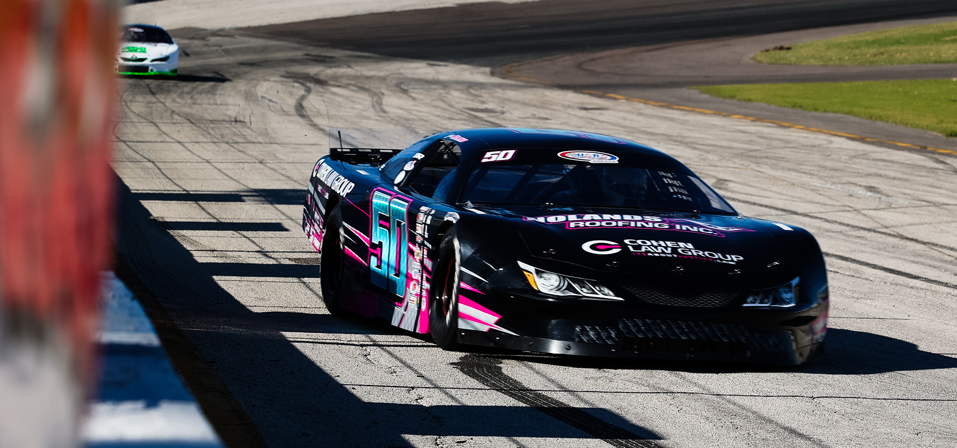 Number 50 Jett Noland racing his Black and pink race car. speeding on the Freedom Factory track under the bright lights during a the Bill Bigley Memorial 128, showcasing the excitement of professional racing.