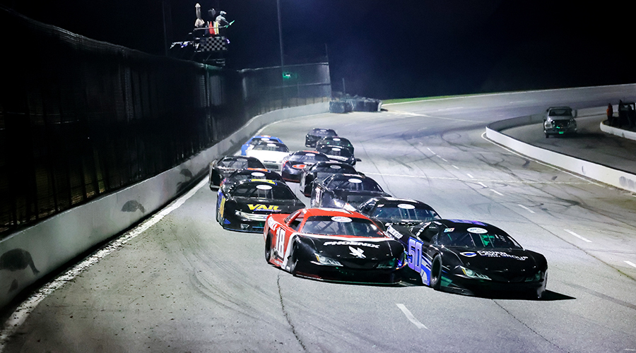 Action shot at Cordele Motor Speedway featuring Jett Noland Motorsports – A group of race cars, including the #18 car from Jett Noland Motorsports, speeds around the track under the lights at Cordele Motor Speedway. The intense racing action highlights the competitive atmosphere of the event